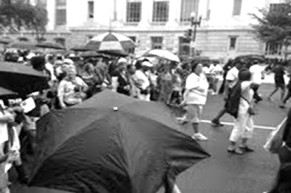 Black and white showing a crowd of people walking in downtown D.C. Some are carrying umbrellas.