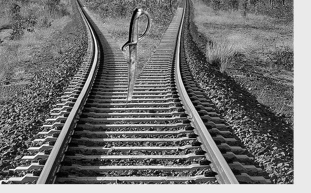 A sword stuck between two diverging train tracks.