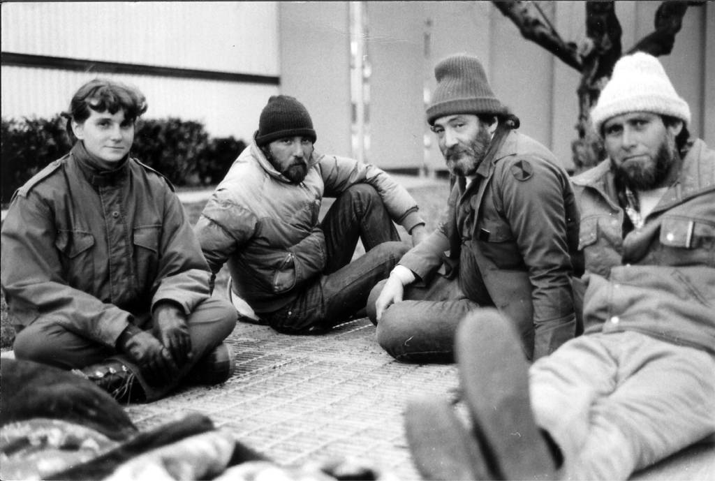 Black and white photo of four people sitting on the ground, wearing cold-weather clothes.