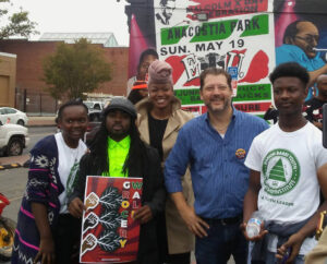 Councilmembers Trayon White and David Grosso pose with three rally attendees in front of a colorful Anacostia Park mural