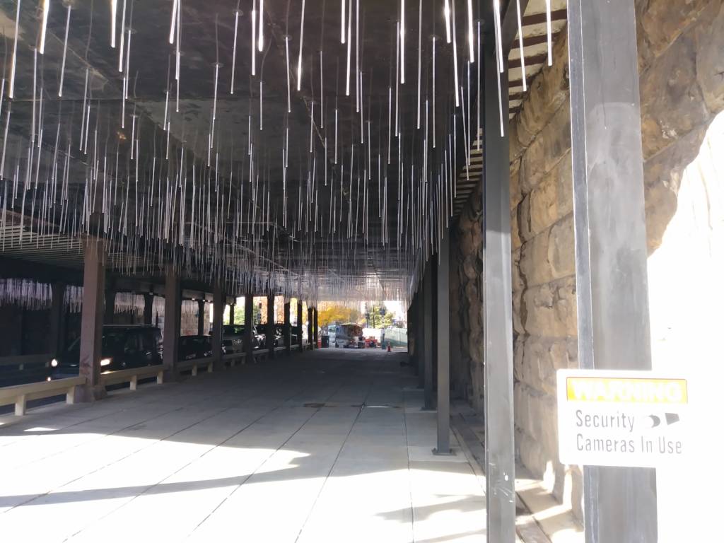 Photo of the M Street NE underpass with white thin light sticks jutting down from the ceiling and a security camera notice posted in the foreground.