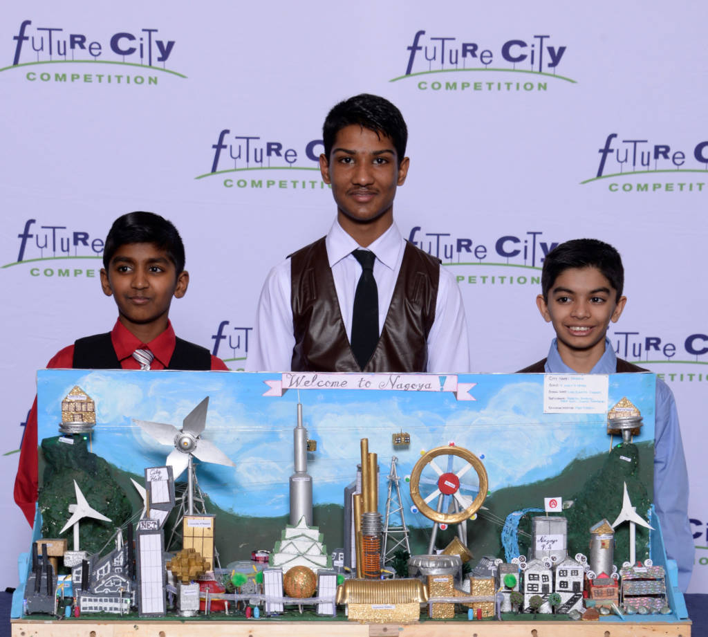 Photo of three students stand behind a diorama of their city.