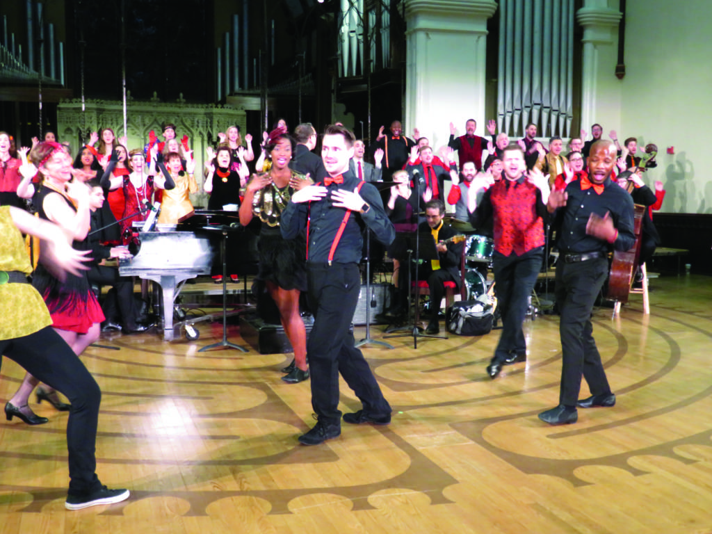 Photo of performers dancing in front of a chorus and several musicians.