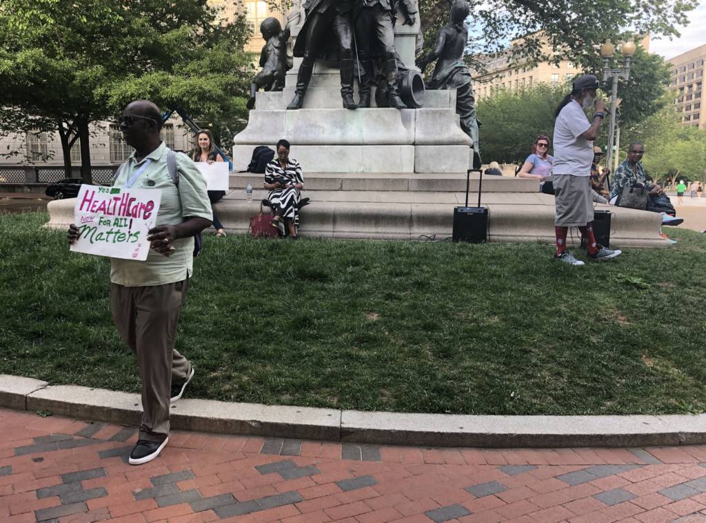 Photo of an activist holding a sign in front of a statue in Lafayette Square
