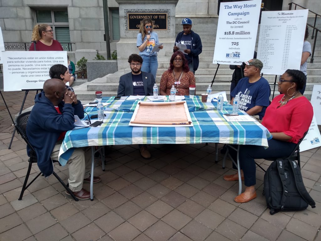 Photo of a mock council session held by homelessness advocacy groups in front of the Wilson Building.