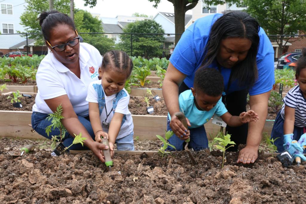 Photo of two children handling garden tools and digging in a planting bed.