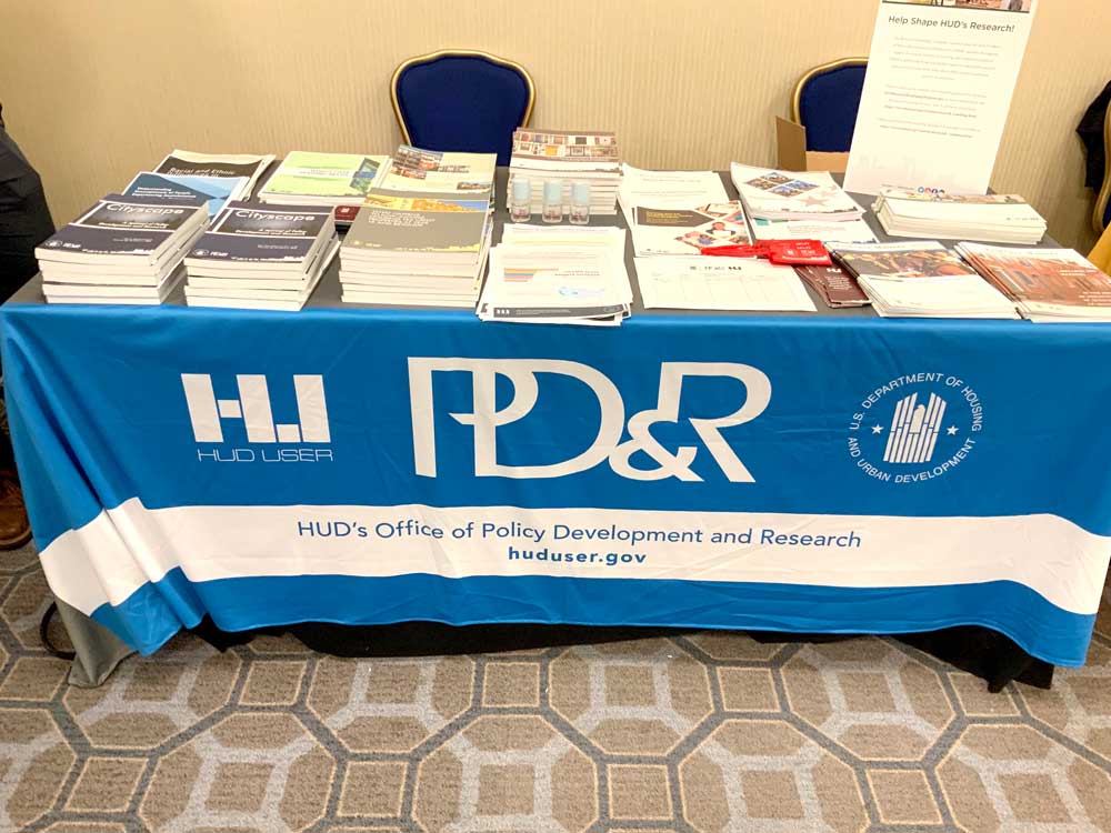 photo of a table with "HUD User" "HUD Exchange" and "PD&R" logos on it, with stacks of papers and booklets on top.