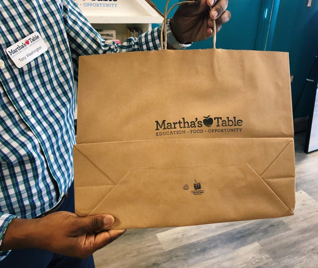 Photo of a man holding a brown paper bag that bears the Martha's Table logo