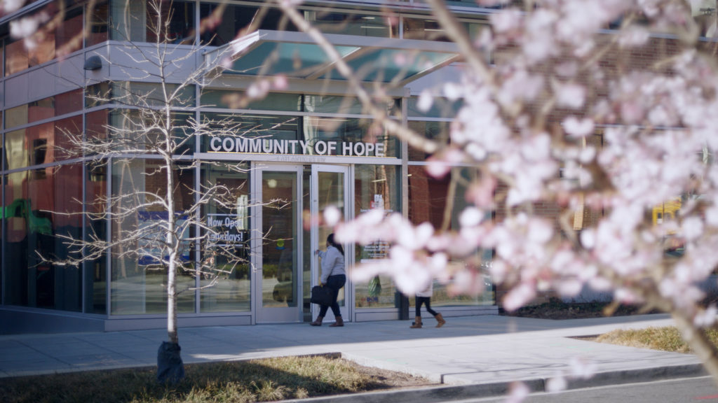 Photo of people walking into one of Community of Hope's locations, as scene through a flowering tree.