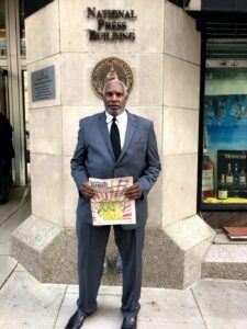 Wendell Williams standing in front of the National Press Building holding a Street Sense paper.