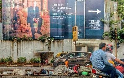 People experiencing homelessness seen laying out in front of a sign that says a new Trump Tower is being built down the road from them.