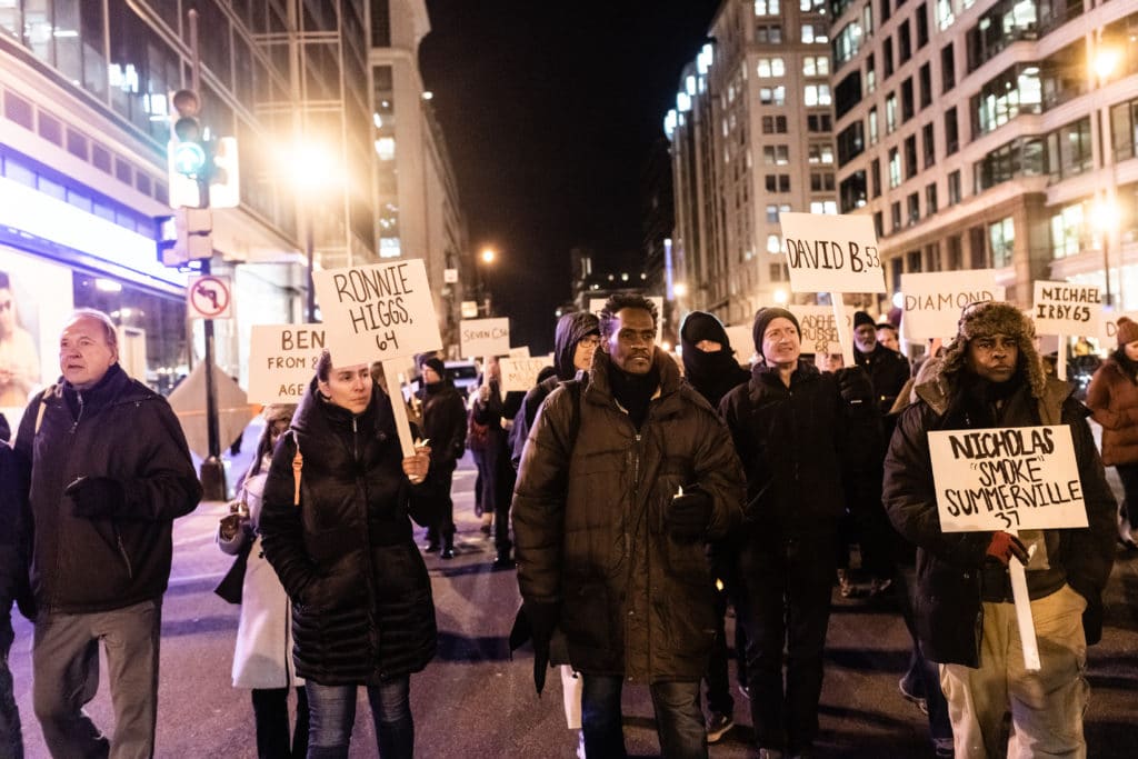Photo of parchers in the street, holding signs bearing the names and ages of people who died without a home that year.