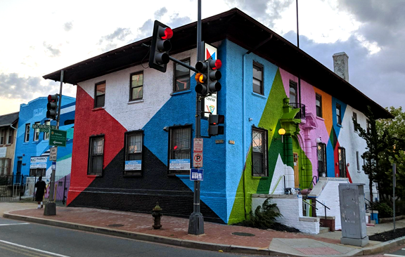 A building painted with a colorful mural on the side. A traffic light stands in front of the building
