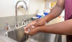 An African-american person wearing a red shirt washes their hands. Only their torso, arms, and hands are visible in the photo