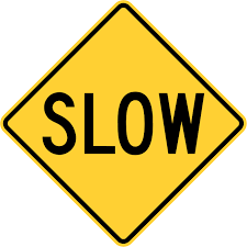 A yellow diamond shaped road sign with the word "slow" on it in black lettering. The sign also has a black border.