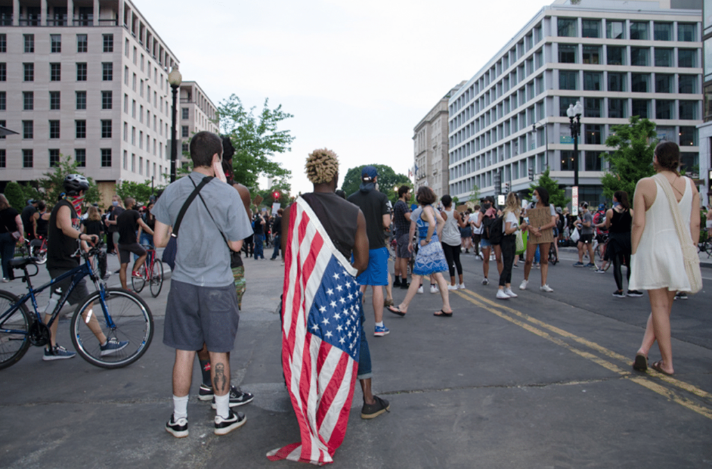 Photo showing a young person with their back facing the camera, draped in an American flag in downtown DC.