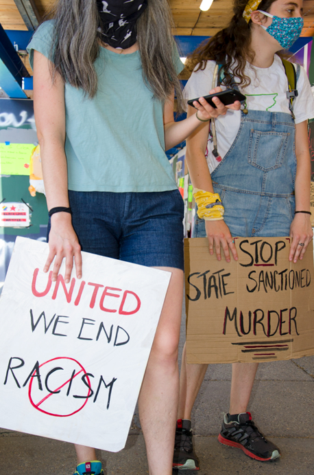 Photo of two young white women holding signs that say "United we end racism" and "stop state-sponsored murder"