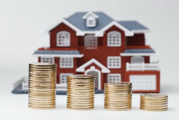 Photo of coins stacked in from of a model house