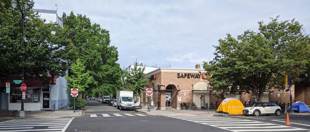 Photo showing Cairo Wine and Liquor on the left side of Corcoran Street NW and Safeway on the right, with a yellow tent and two blue tents visible in front of Safeway.