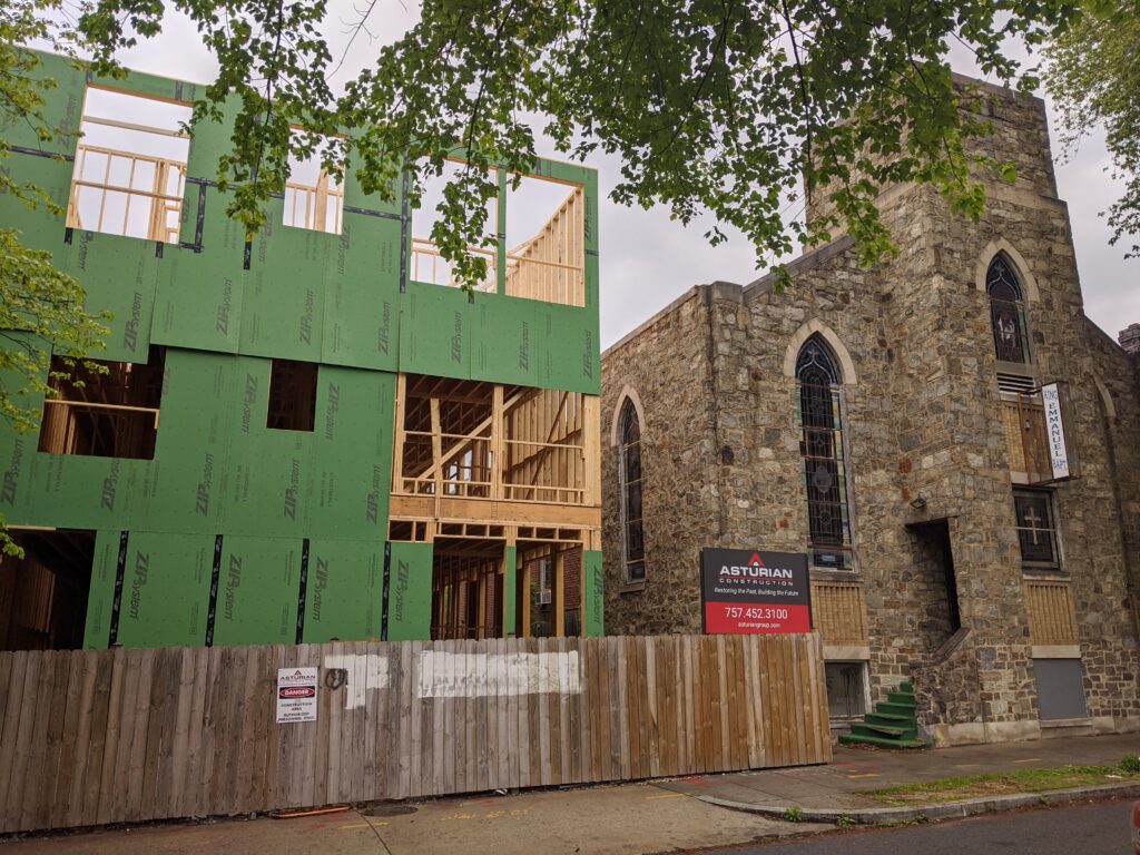 Photo showing a fenced-off construction area where a full structure has been erected, with unfinished walls masked in a green material.