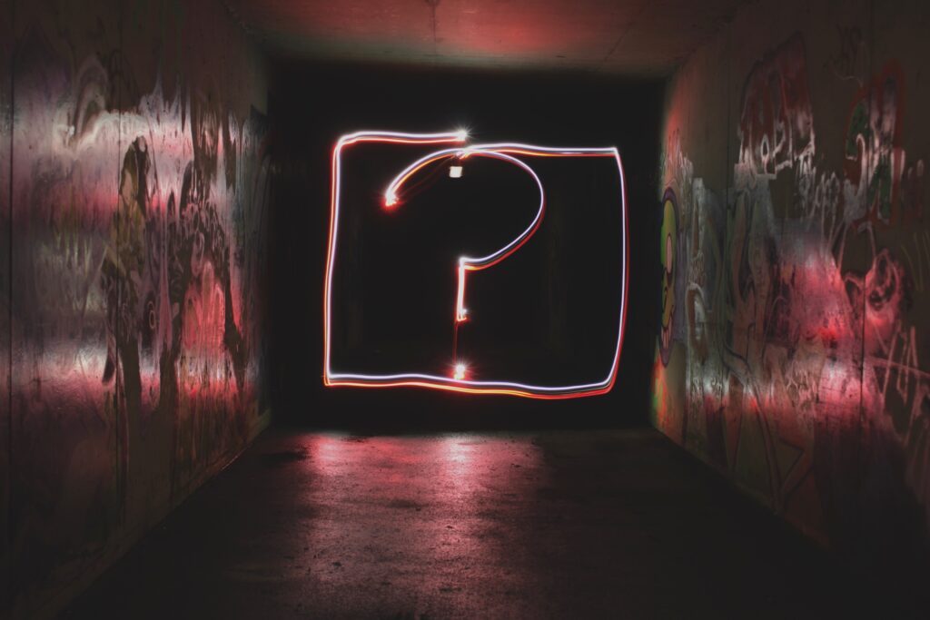 Phot of neon lights in the form of a question mark in a dark room