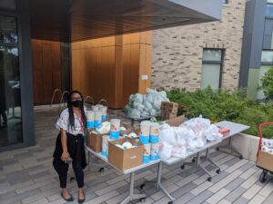 A Black woman stands next to a table filled with bags of food.