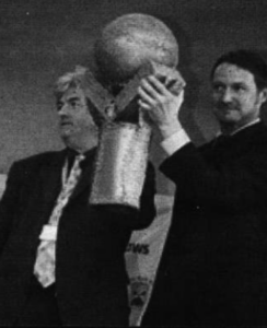 A photo of two men holding up a trophy.