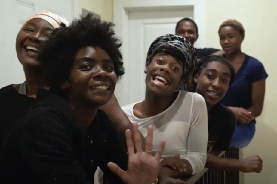 Image shows six women smiling and laughing in a home. There is a door behind them.