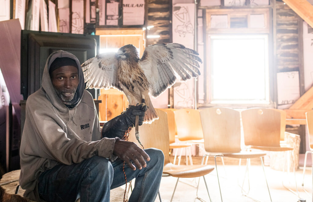 Rodney S. sitting down holding Raven with his wings open