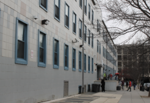 Photo displays the CCNV entrance, a white building with blue windows, residents are gathered outside
