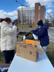 Photo of two woman standing at opposite sides of a portable table in a patch of grass. A coat is being passed between them.
