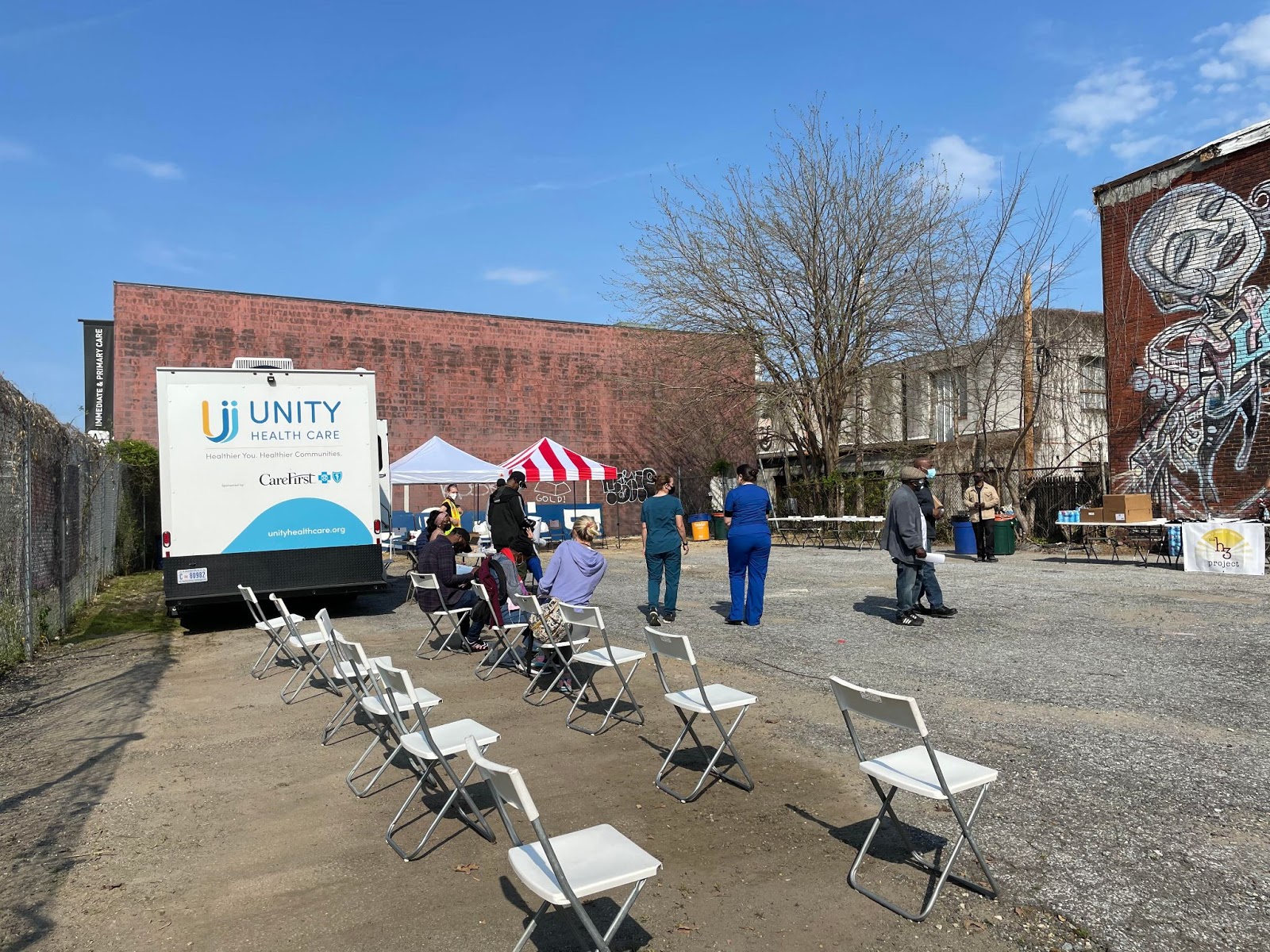 Image shows chairs, Unity Health Care truck and scattered people in a parking lot in NOMA