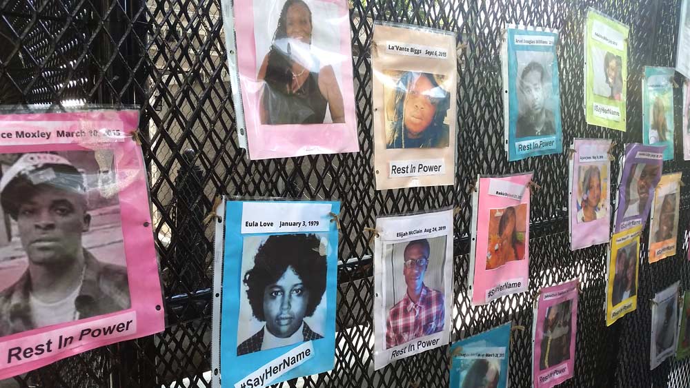 Photo showing brightly colored pieces of paper tacked to the fencing at Lafayette Square. Each sheet bears the name and hpoto of a person who was killed by police.