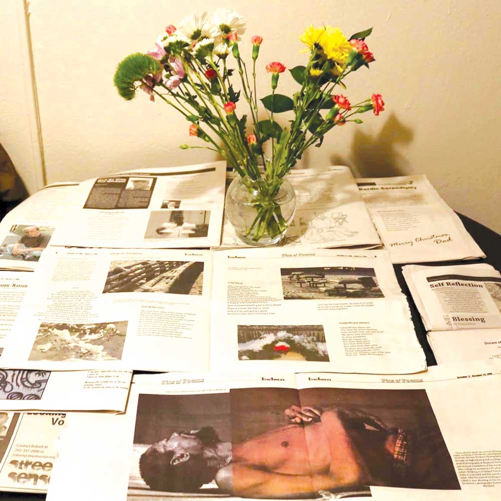 Photo showing open newspapers layered over each other and arranged in a very particular way. A vase of flowers sits on top of them.