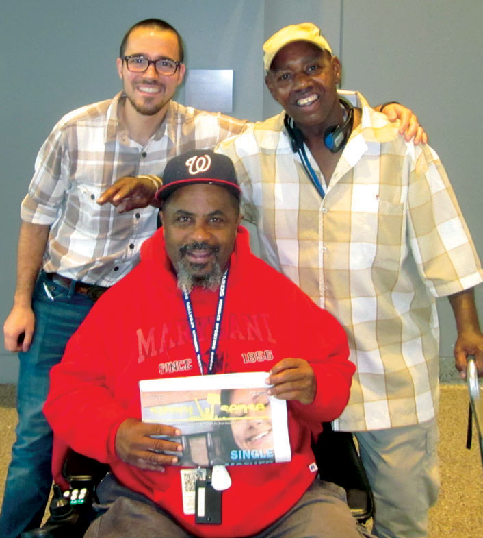 Photo showing three people posing together, one of whom is holding a Street Sense newspaper.