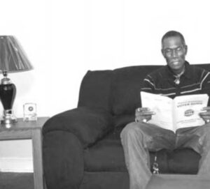 Photo of Tommy Bennett sitting on his couch, reading a book.