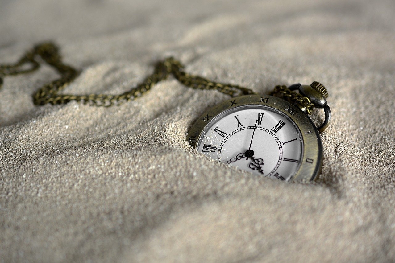 Photo of a pocket watch partially buried in sand.