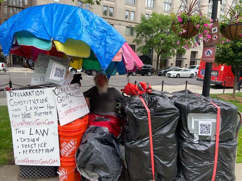 The photo depicts Kingery sitting by his belongings, all tightly packaged to protect them. He has signs discussing government on the outside of them.