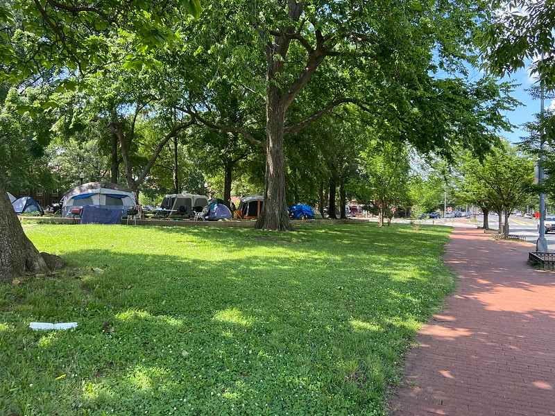 Numerous tents, tables, chairs, and a grills are set up in the encampment at the park.