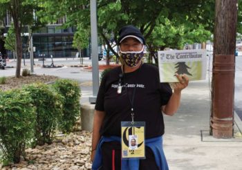 Photo of a vendor for The Contributor holding up a newspaper