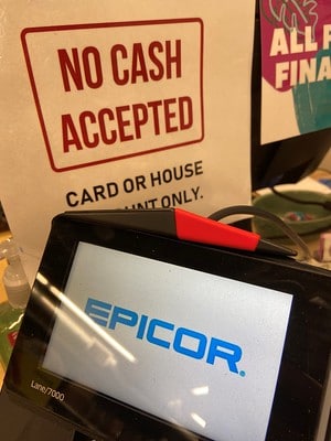 A "No Cash Accepted" sign is displayed in front of a point of sale terminal