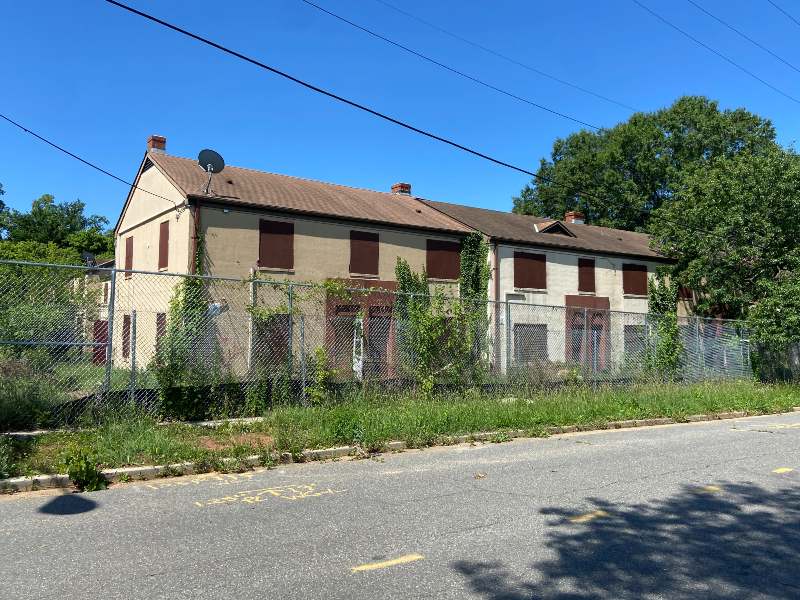 Metal fencing surrounds two adjoining homes that are boarded up and in disrepair.