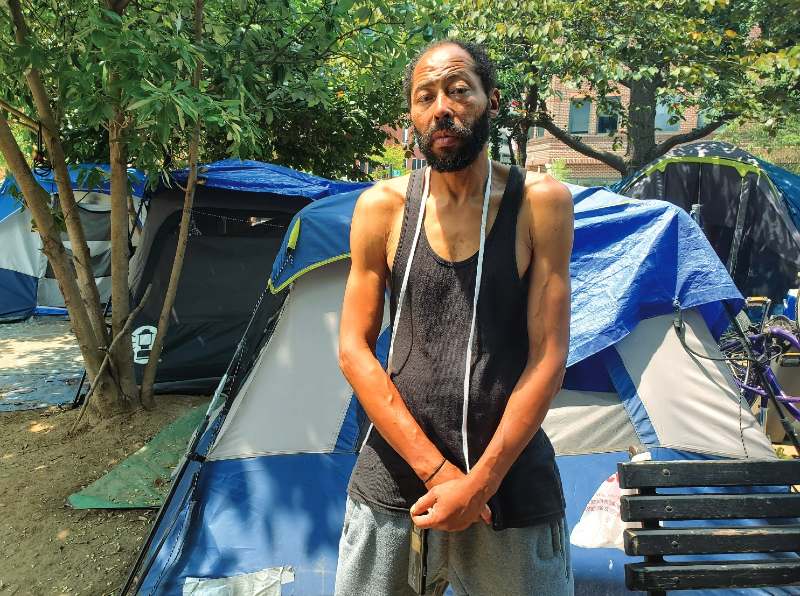 Woodson stands in front of his tent; numerous other tends are behind his