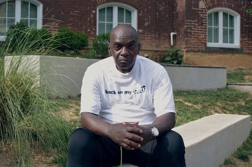 Ronald E Armstrong sits on a bench outside a brick building