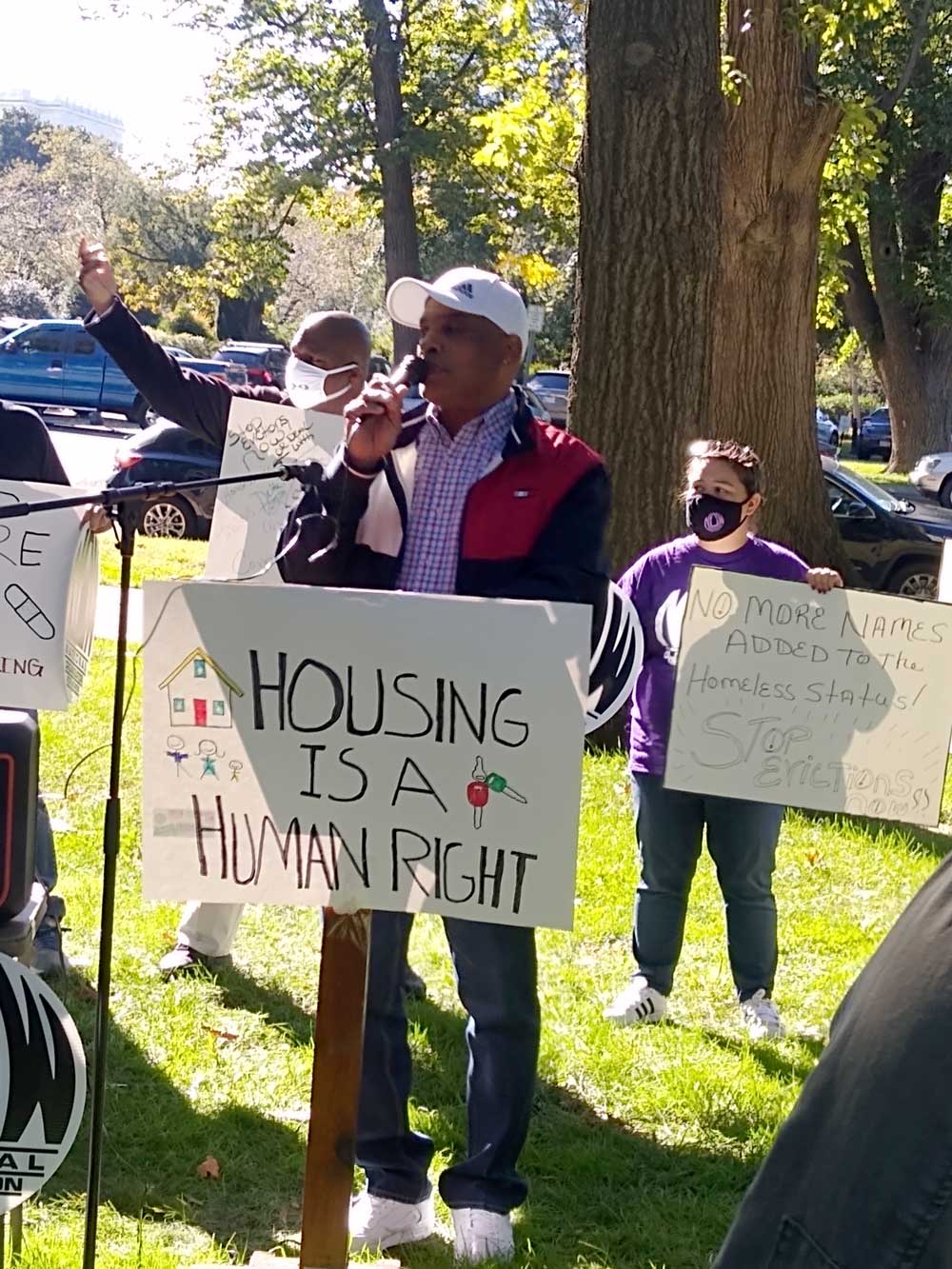 A man stands at a podium that bears the sign "housing is a human right"