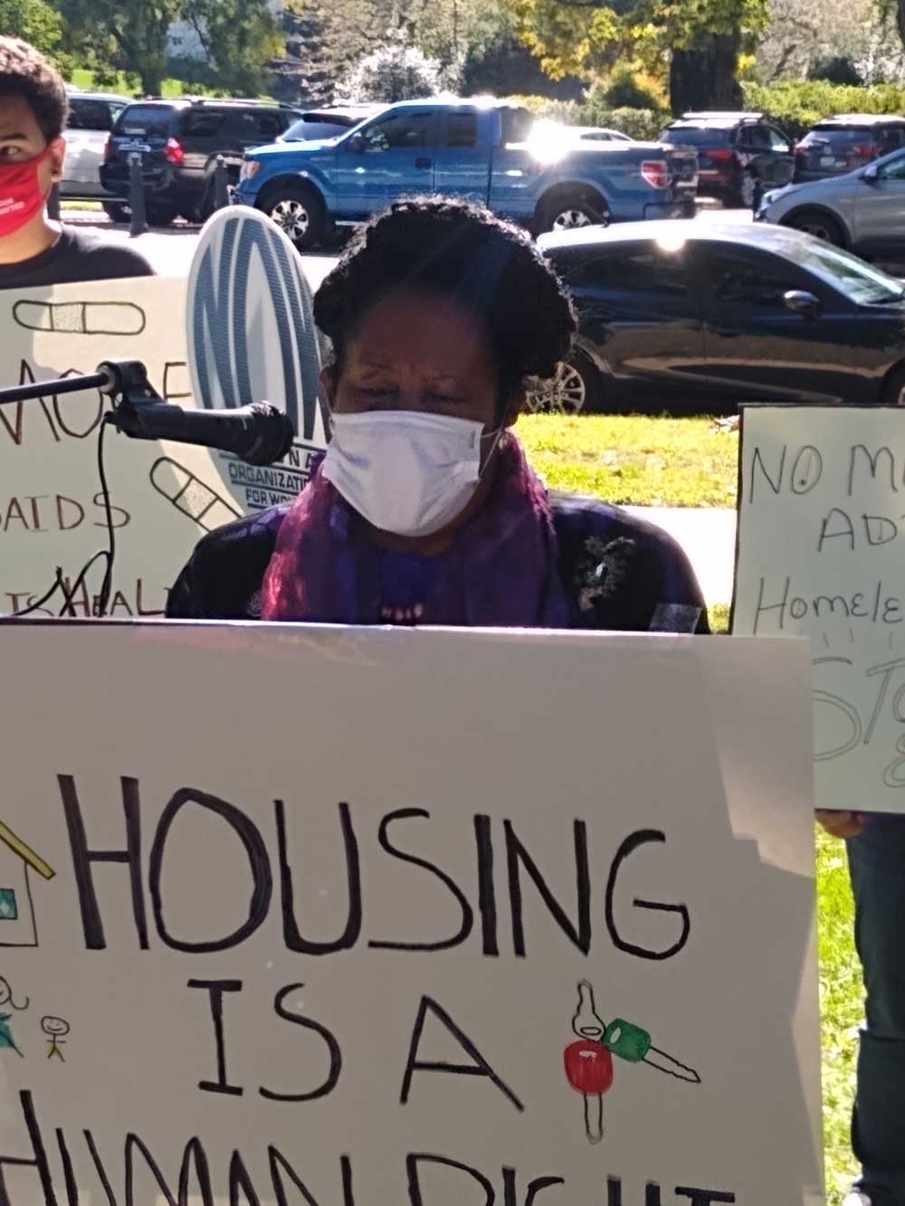 Photo of a woman speaking at a podium that bears a sign reading "housing is a human right"