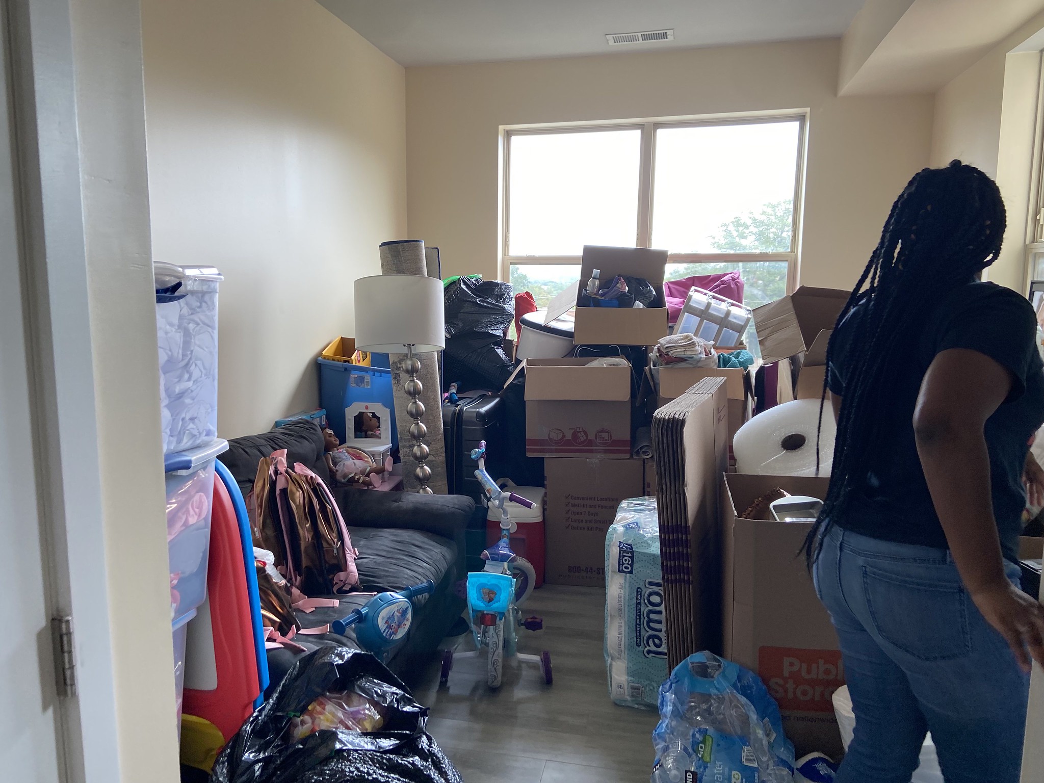 A woman stands in a room filled with boxes and various belongings.