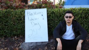 A young man sits next to a whiteboard sign that says "Blackburn Takeover Day 24!"