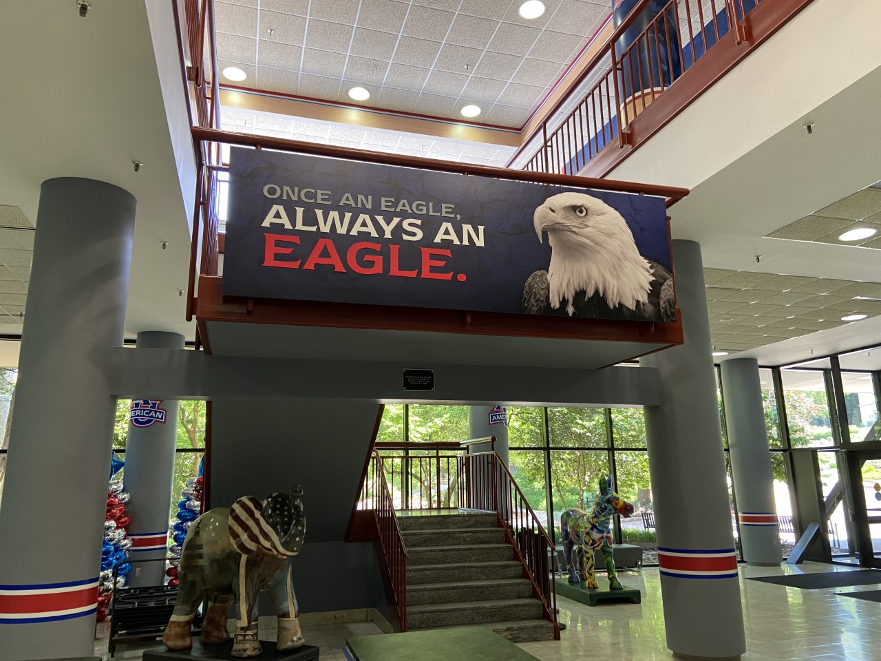 A photo of the inside of American University. Above a staircase is a poster that says, "Once an eagle, always an eagle" with a bald eagle on the side. 