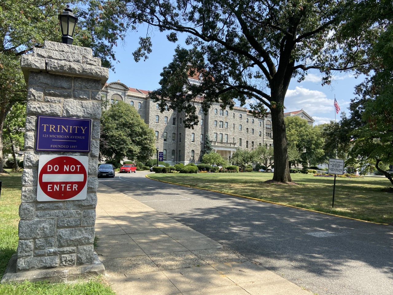 A photo of the outside of Trinity Washington University. In the foreground, a column with a "Do Not Enter" sign and a Trinty University plate stands.